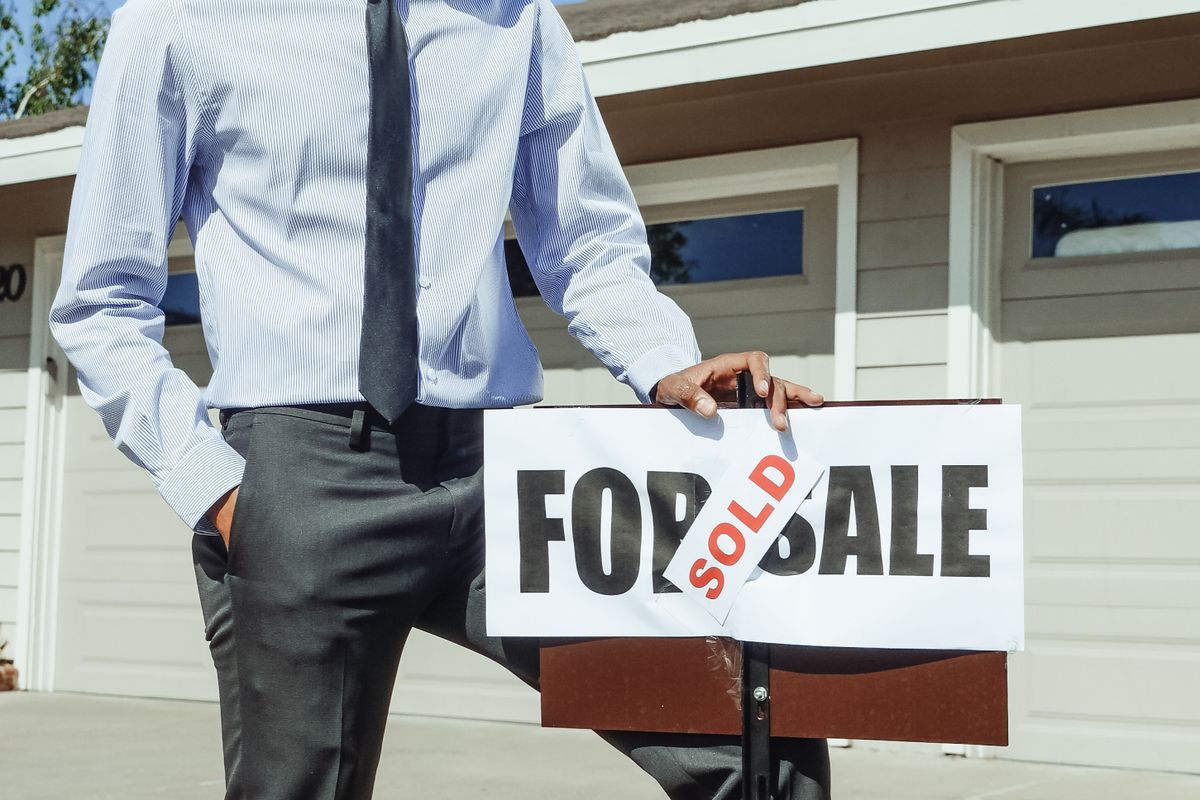 A real estate professional standing beside a sold sign in front of a home