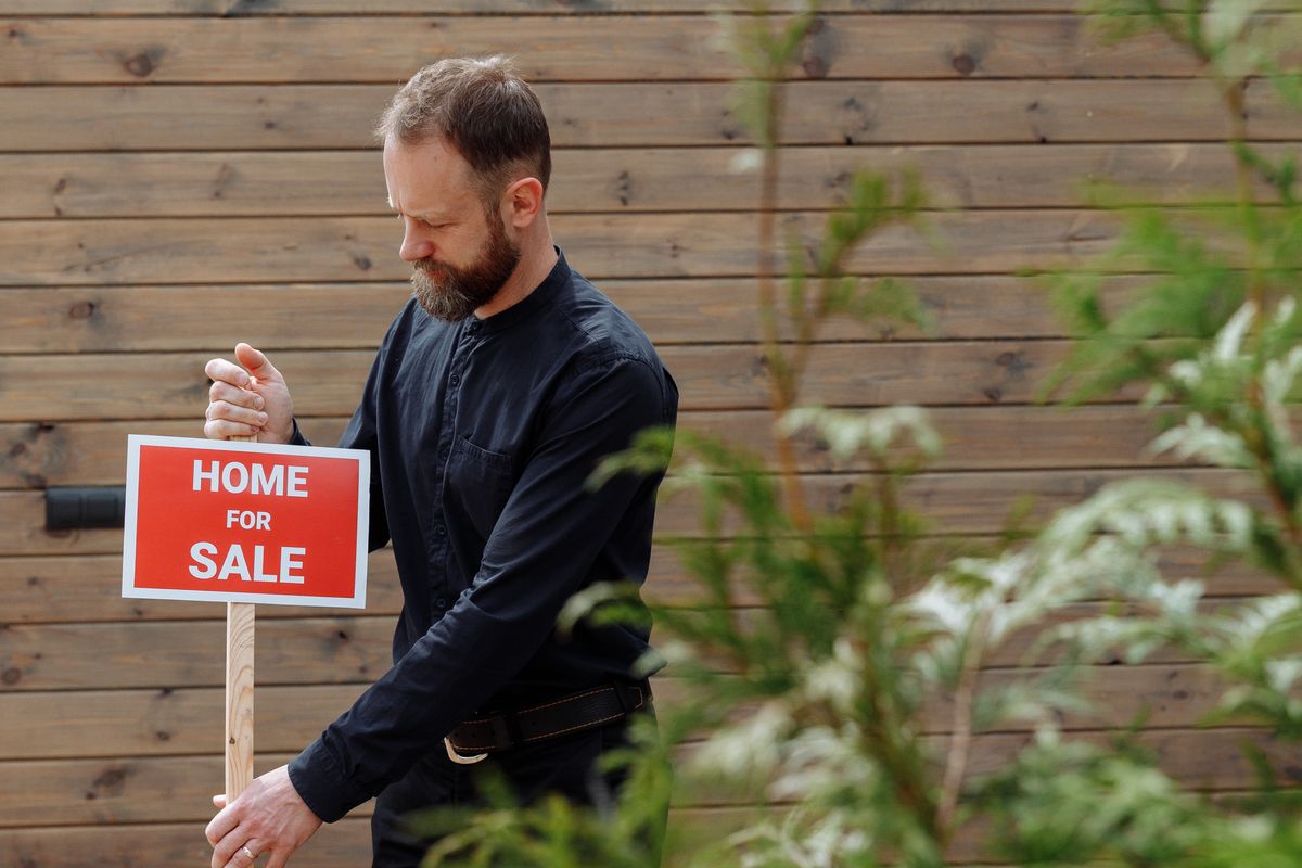 A real estate agent standing in front of a home with a listing sign